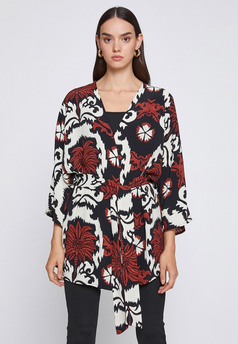 Top estilo kimono en negro, blanco y rojo con un patrón floral, que presenta un escote en V, cintura ceñida y mangas de tres cuartos. Textura de tejido suave.