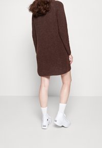 Abito marrone lavorato a maglia con maniche lunghe, una vestibilità rilassata e un collo rotondo, abbinato a sneaker alte bianche e calzini alla caviglia.