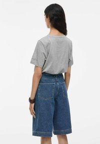 Maglietta grigia a maniche corte abbinata a pantaloni shorts in denim blu a vita alta, con due tasche posteriori e orlo risvoltato.