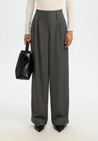 Pelēkas piegrieztas bikses ar krokām, augstu jostasvietu, platas kājas un gludu faktūru. Kombinētas ar melnu ādas somu un melniem smailiem apaviem.
