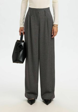 Szare, dopasowane spodnie z zakładkami, z wysokim stanem, szerokimi nogawkami i gładką fakturą. Połączone z czarną skórzaną torbą i czarnymi, spiczastymi butami.