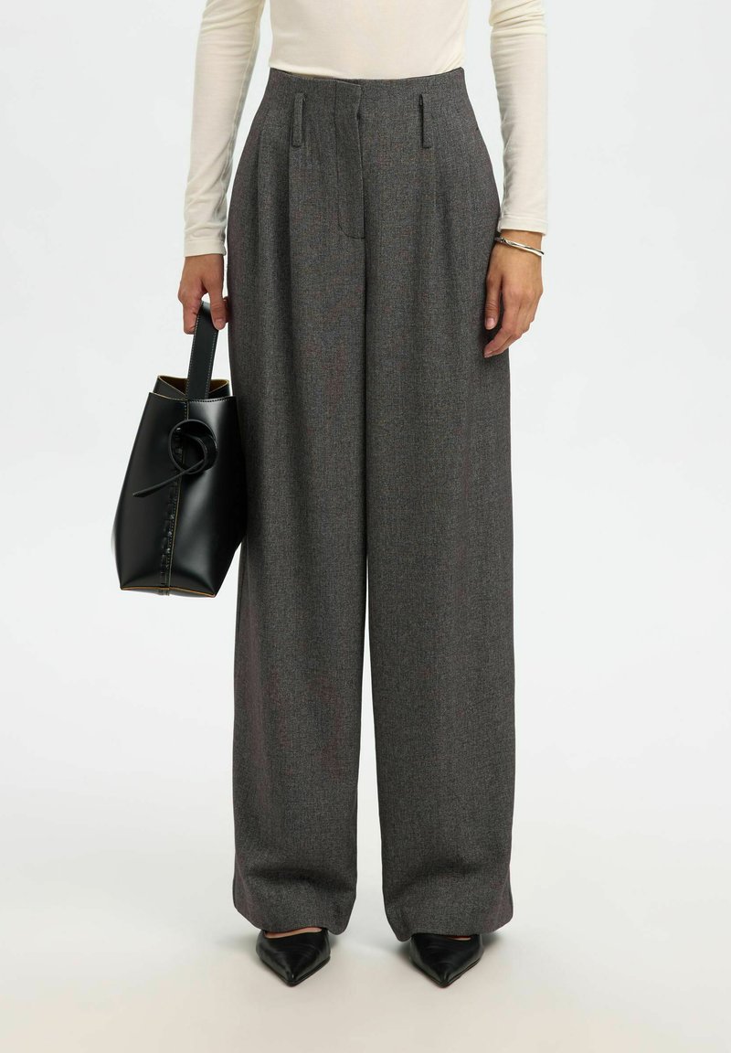 Pelēkas piegrieztas bikses ar krokām, augstu jostasvietu, platas kājas un gludu faktūru. Kombinētas ar melnu ādas somu un melniem smailiem apaviem.