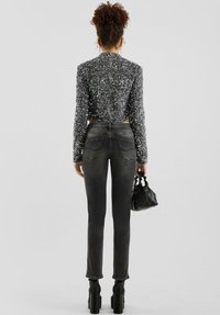 Krótka czarna kurtka z cekinami zapinana na zamek z tyłu, zestawiona z ciemnymi dopasowanymi jeansami. Dodatki to czarna torebka i botki na masywnym obcasie.