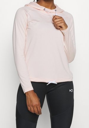 Osoba ubrana w jasnoróżową bluzę z kapturem z długim rękawem oraz czarne legginsy z małym białym logo na górnej części uda.