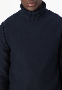 Marineblå høyhalset genser med ribbestrikket krage. Teksturert strikket stoff, tettsittende design, synlige sømdetaljer på skuldrene.