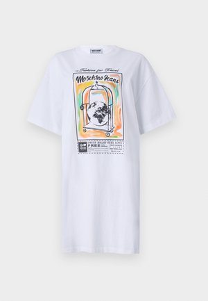 White cotton oversized t-shirt featuring a colorful graphic print of a luggage cart with a globe, text, and bold outlines. Short sleeves.