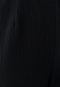 Sort tekstureret stof med et ribbet mønster, der har subtile variationer i overfladedybde. Materialet virker blødt og let elastisk.