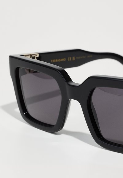 Black oversized sunglasses with thick, angular frames. Dark lenses with a smooth finish and subtle branding on the inner arm.