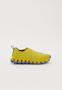 Sapatilha atlética amarela em malha com sola segmentada única em amarelo e azul, design de atacadores e tab de puxar azul no calcanhar.