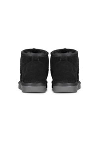 Botas de tobillo de ante negro con un suave forro interior, que presentan una parte trasera texturizada y una suela de goma plana. El diseño es minimalista, sin logotipos visibles.