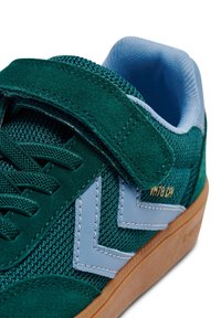 Zielone sneakersy z zamszu i siateczki, z jasnoniebieskim akcentem i brązową gumową podeszwą, wyposażone w rzep i wzór w jodełkę.