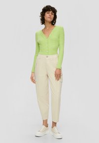 Cardigan en maille verte à manches longues avec un col en V et une fermeture à boutons, associé à un pantalon cargo crème et des baskets compensées beiges.