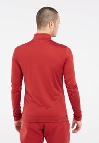 Crveno polo majica s dugim rukavima, visokim ovratnikom, prilagođenim dizajnom, glatkom teksturom i minimalnim brendiranjem na rubu. Prikazan stražnji pogled.