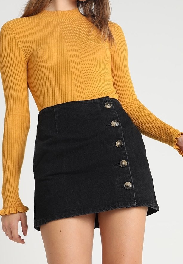 Ribbed long-sleeve top in mustard yellow paired with a black denim skirt featuring a diagonal cut and five brass buttons down the front.