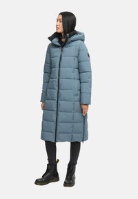 Dugi, svijetloplavi zimski kaput od šuškavog materijala s patentnim zatvaračem sprijeda, kapuljačom i dva bočna džepa, nosi se s crnim čizmama i hlačama.