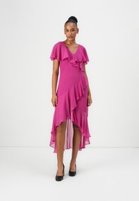 Robe fuchsia avec des manches courtes à volants et un ourlet en couches haut-bas. Fabriquée en tissu léger, elle présente un décolleté en V et une silhouette évasée.