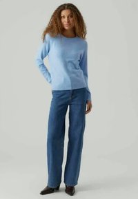 Pulover tricotat de culoare albastru deschis, cu guler rotund, mâneci lungi și manșete cu nervuri, purtat cu blugi dark blue cu talie înaltă și picioare largi, împreună cu botine negre.