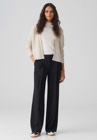 Beige textured cardigan, white turtleneck, black wide-leg trousers, and black sneakers with white soles. Simple, modern outfit.