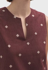 Top sans manches bourgogne avec un col en V, arborant une broderie en forme de diamant blanche et une texture à rayures verticales tout au long.