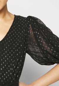 Black dress with sheer puff sleeves, featuring a pattern of shiny silver dots. V-neck design highlights the neckline.