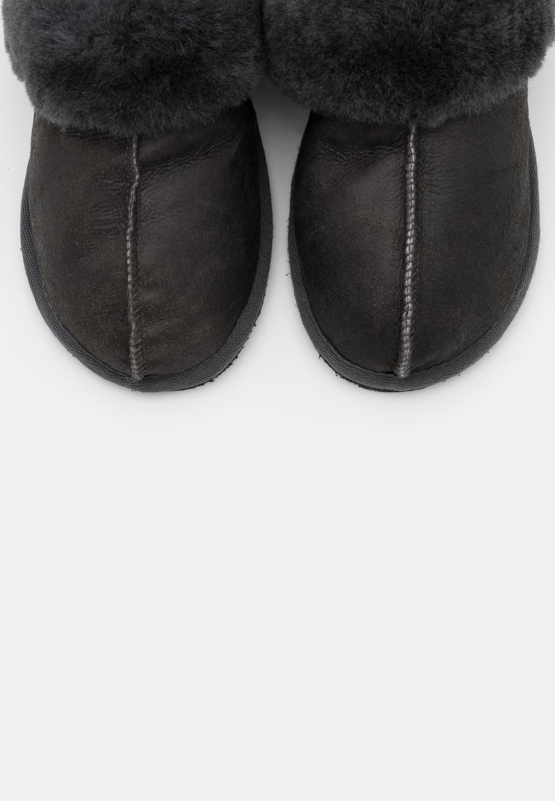 Schwarze Lederslipper mit grauem Fellfutter, abgerundeter Spitze und gestickter Naht. Flache Sohle mit gummiertem Rand. Strukturiertes Material.