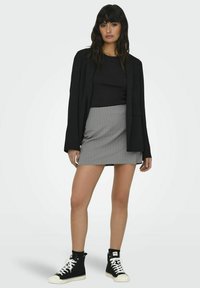 Blazer nero sopra una maglietta nera, abbinato a una mini gonna a righe grigie. Sneakers alte nere completano l'outfit.