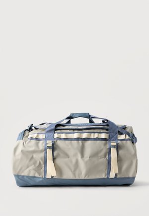 Μεγάλη γκρι και μπλε τσάντα duffel με μπεζ λουριά και χερούλια, τοποθετημένη πάνω σε απλό φωτεινό φόντο.