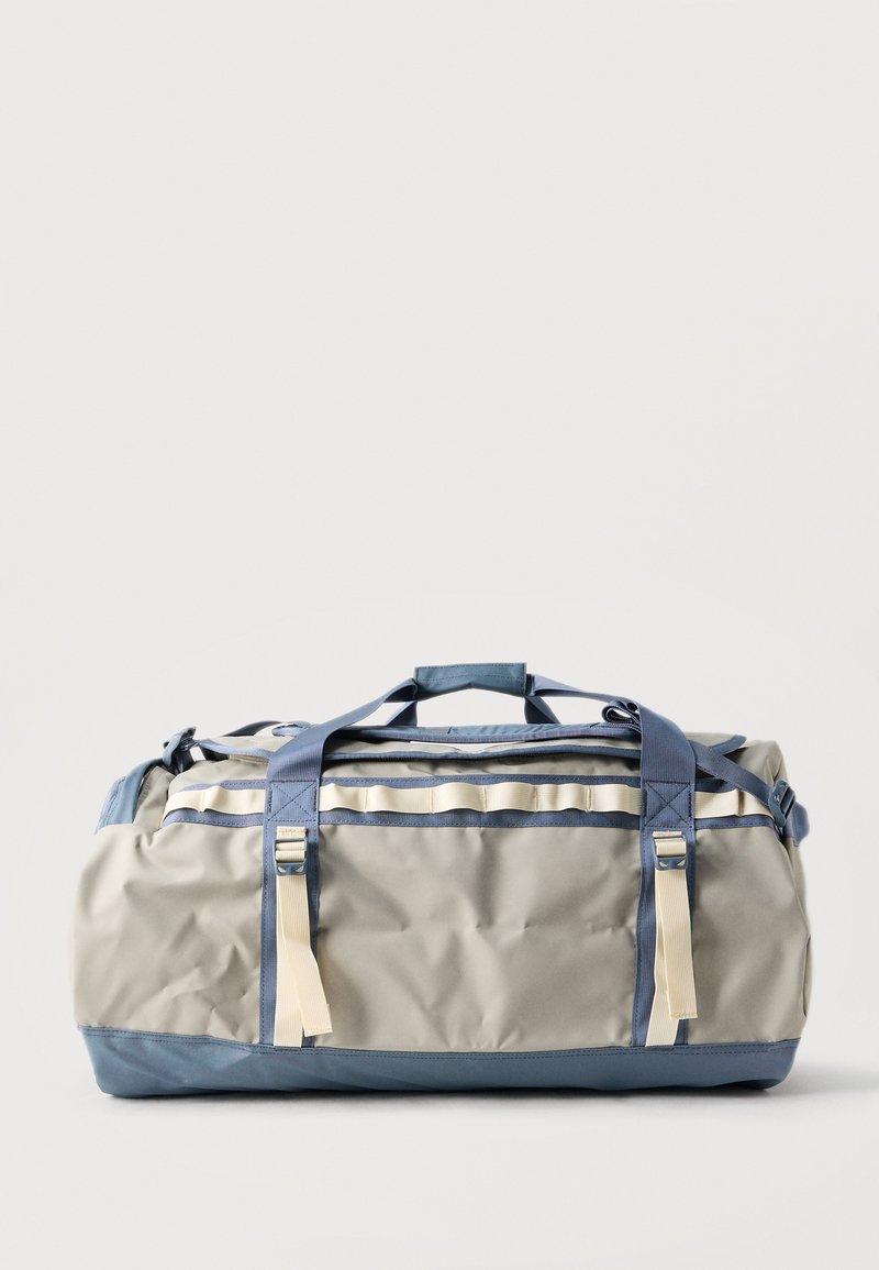 Μεγάλη γκρι και μπλε τσάντα duffel με μπεζ λουριά και χερούλια, τοποθετημένη πάνω σε απλό φωτεινό φόντο.
