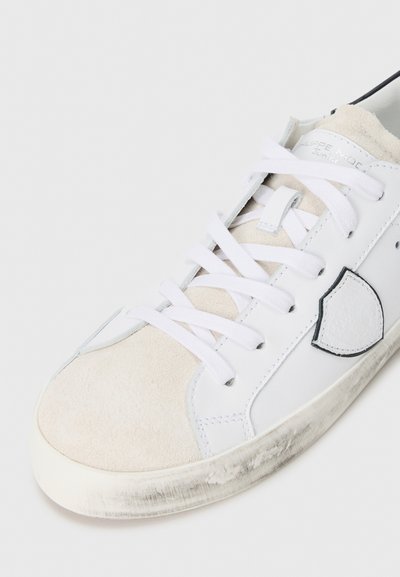 Białe sneakersy z zamszowym noskiem i skórzaną cholewką, białe sznurówki i czarny akcent w okolicy pięty. Lekko zużyta podeszwa.