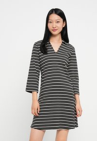 Czarna i biała sukienka w paski z dekoltem w serek i rękawami 3/4. Wykonana z lekkiego materiału, z luźnym krojem.