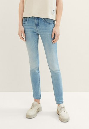 Hellblaue Jeans aus Denim mit schmaler Passform, ausgestattet mit vorderen Taschen, einer mittelhohen Taille und dezenten Used-Effekten. Kombiniert mit beigen Sneakers.