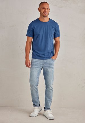 Blue cotton t-shirt with a round neckline, short sleeves, and light blue denim jeans. Worn with white sneakers featuring gray accents.
