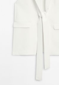 Witte mouwloze vest met een striksluiting, twee voorzakken en een gladde textuur, met een gestructureerd ontwerp en een minimalistische stijl.