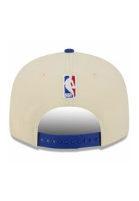 Cream baseball cap with a flat brim and a blue adjustable strap. Features an embroidered NBA logo in red, white, and blue on the back.