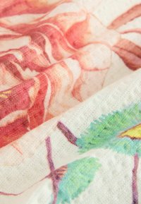 Barevná česaná bavlněná látka s květinovými vzory ve světlých odstínech růžové, bílé a zelené, s texturovaným povrchem. Viditelné jsou tři vrstvy.