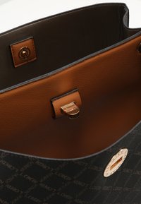 Black patterned tote bag with textured exterior, brown leather interior, and a gold-tone clasp. Features brand logo and smooth finish.