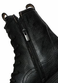 Botas de tobillo de cuero negro con un acabado texturizado, que presentan cordones en la parte delantera, un cierre lateral y lengüetas en bucle para facilitar su uso.