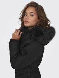 Black parka jacket with a fur-lined hood, cinched waist, and elastic cuffs. Features a badge on the arm and a smooth, textured fabric.