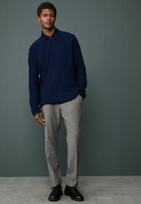 Navy long-sleeve polo shirt with a collar, paired with light gray tailored trousers and black leather shoes. Smooth fabric and fitted design.