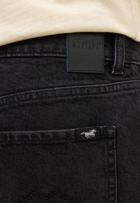 Melnu denim bikses ar ādas Mustang etiķeti jostas vietā un mazu zirglogo aizmugurējā kabatā. Gluda tekstūra.