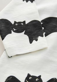 Tela de algodón con un estampado de murciélagos en blanco y negro. El diseño incluye ilustraciones de murciélagos juguetonas con expresiones faciales distintas.