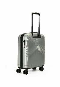 Silberner Hartschalenkoffer mit einem strukturierten Zickzackmuster, ausziehbarem schwarzen Griff und vier schwarzen Rollen für Mobilität. Mit Reißverschluss.