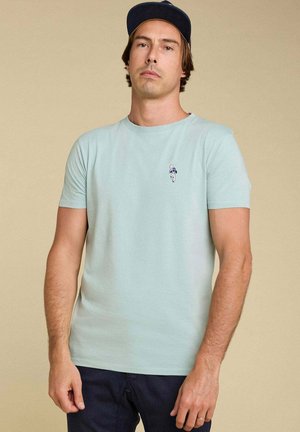 T-shirt en coton bleu clair avec des manches courtes, un col rond et un petit motif brodé sur la poitrine. Design simple et décontracté.