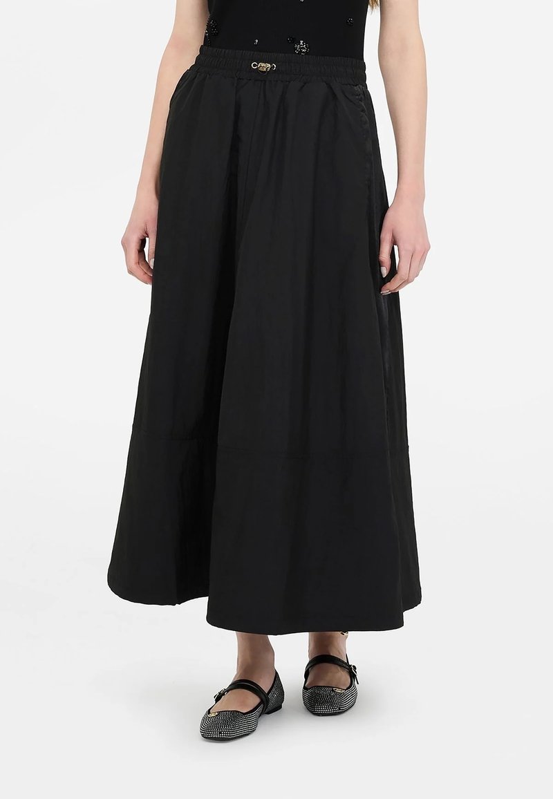 Gonna lunga nera in tessuto liscio, con vita elastica e design a balze sottili, abbinata a ballerine nere con motivo.