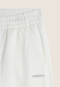 Pantalons de survêtement blancs avec taille élastique et poches latérales. Présente un logo brodé subtil "FREDDY" en argent en bas à droite. Texture de tissu douce.