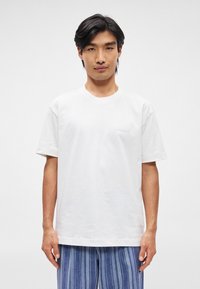 Λευκό βαμβακερό μπλουζάκι με στρογγυλή λαιμόκολα, κοντά μανίκια και �μικρή τσέπη στο αριστερό στήθος. Λείος υφασμάτινος χαρακτήρας, άνετη εφαρμογή.