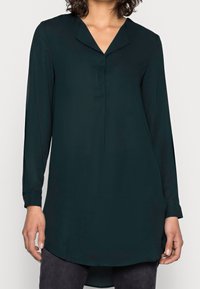 Mörkgrön långärmad tunika med V-ringning och knappade manschetter. Tillverkad av mjukt tyg, med en böjd nederkant och minimala sömmar.