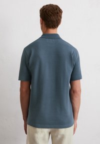 Polo a maniche corte in tessuto blu scuro testurizzato, con colletto a punta e vestibilità rilassata. Dettagli di cucitura discreti vicino all'orlo.