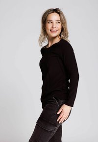 Schwarzes, geripptes Langarmoberteil mit Rundhalsausschnitt und subtilen strukturierten Nähten, kombiniert mit dunkelgrauen Cargo-Hosen, die über Taschen und einen lässigen Schnitt verfügen.