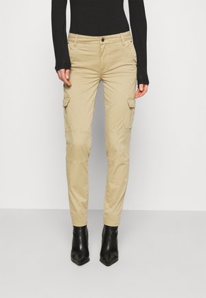 Beige slim-fit cargo pants with flap pockets worn with black long-sleeve top and black pointed-toe ankle boots on grey floor.